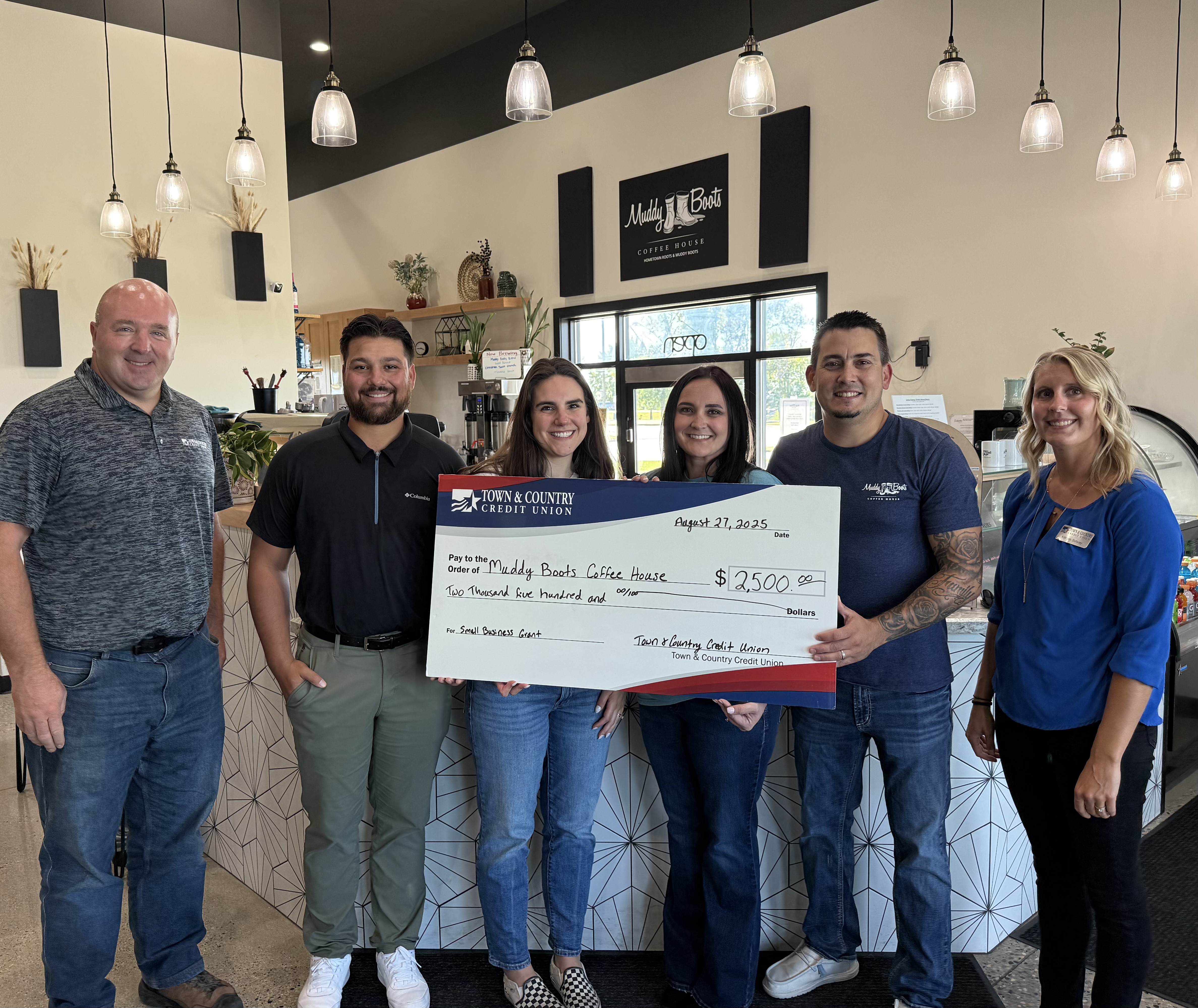 Group of people holding a large check in a coffee house.